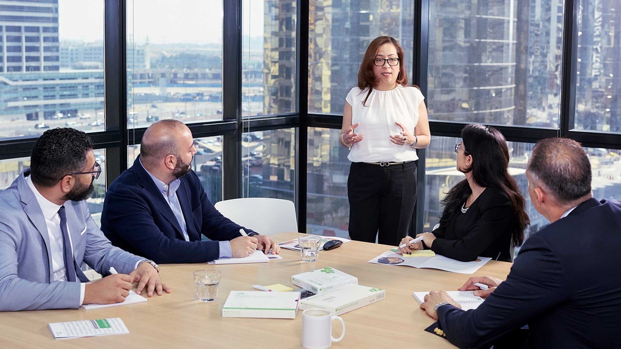 Several employees listening to a woman leader in an office meeting